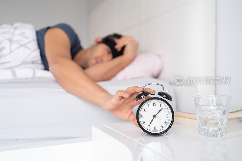 Young Man Reaching For Her Alarm Clock After Waking Up İn Bed At Home